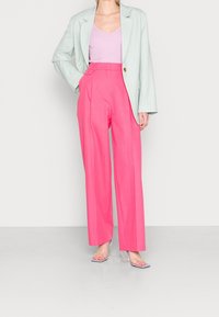 Ljusgrön kavaj, rosa högmidjade byxor med veck och klara blockklackade sandaler. Kavajen har en enda guldklicka.