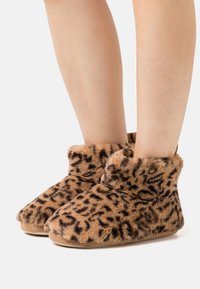 Brown leopard print cozy slippers with a plush, furry texture and a cuffed top. Soft soles provide comfort and warmth for indoor use.