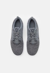 Harmaat urheilukengät, joissa on teksturoitu neulottu päällinen, pyöreä kärki, vaaleammat harmaat yksityiskohdat ja joustava valkoinen pohja.