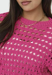 Roze gebreide trui met open lattice patroon, voorzien van een ribgebreide halslijn en korte mouwen. Accentueert met een gouden ketting.