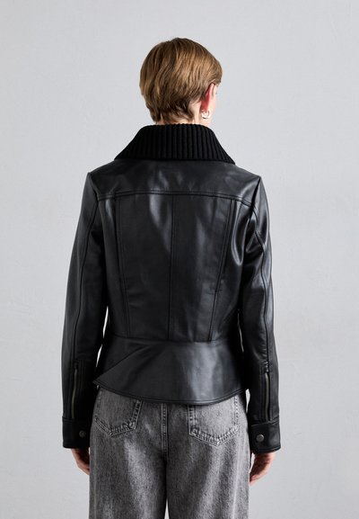Black leather jacket with a ribbed collar, fitted waist, and zippered cuffs. Worn over gray, textured wide-leg pants.