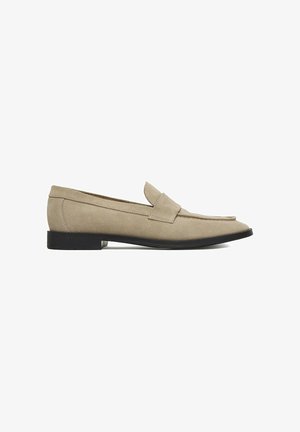 Mocassino in suede beige con suola piatta nera, punta arrotondata e classico dettaglio a fascia per inserire la moneta, mostrato di profilo su sfondo bianco.