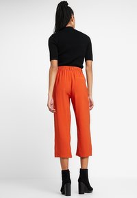 Korte oranje broek met een elastische tailleband, gemaakt van lichte stof. Gecombineerd met een zwart shirt met korte mouwen en zwarte hoge laarzen.