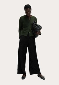 Zielony dzianinowy kardigan, czarne fakturowane spodnie z szerokimi nogawkami, czarna złożona kopertówka i czarne płaskie buty. Dopasowany krój podkreśla miękkie materiały.