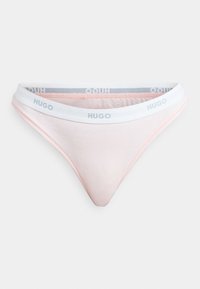 Light pink women's thong with a white elastic waistband featuring "HUGO" logo. Smooth texture with a minimalistic design and triangular shape.
