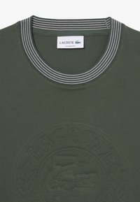 Olijfgroene katoenen t-shirt met een geribde hals in contrasterende strepen. Voorzien van een reliëf Lacoste-logo op de voorkant. Klassieke pasvorm.