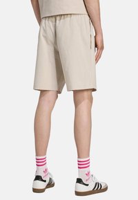 Beiga shorts i textil med struktur, elastisk midja och sidoglittrar. Matchas med svarta och vita sneakers samt rosa randiga strumpor.