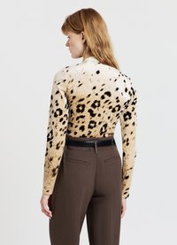 Maglietta a maniche lunghe con stampa leopardata in beige e nero, abbinata a pantaloni marroni con cintura nera e due tasche posteriori.