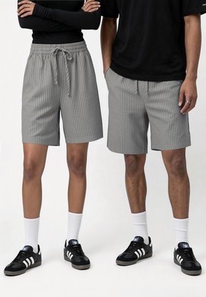 Kaks inimest, kes kannavad halli triibulist nööriga lühikest pükst, musti toppe, valgeid sokke ja musti Adidas tossusid, seisavad kõrvuti.