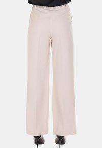 Pantaloni beige a gamba larga indossati con stivaletti neri con tacco alto, mostrati di schiena su uno sfondo semplice.