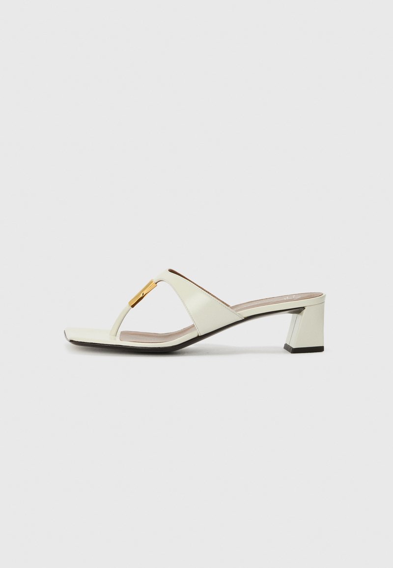 Sieviešu blokveida papēžu sandales gaismas krēmkrāsā ādā ar vienkāršu dizainu. Iezīmē zelta akcentu uz siksniņas un kvadrātveida purngala formu.