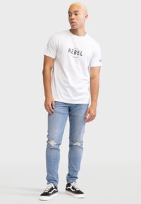 Hvid bomulds-T-shirt med en sort "REBEL" grafik på fronten. Sættes sammen med lyseblå ripped jeans og sorte sneakers.