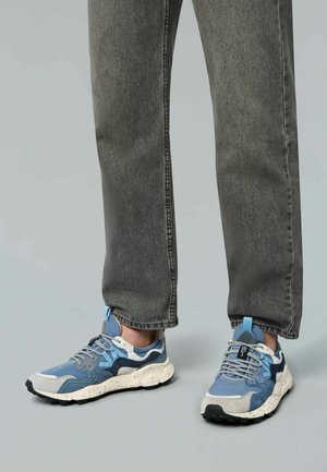 Blaue und graue Sneakers mit einem strukturierten Obermaterial, gesprenkelter weißer Sohle und blauen Akzenten. Getragen mit grauen Jeans.