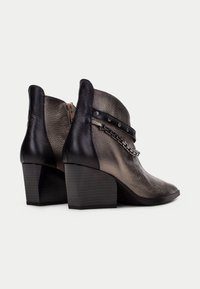Botas de tobillo de cuero con un esquema de color gris metálico y negro, un tacón de bloque y acentos decorativos de cadena con tachuelas.