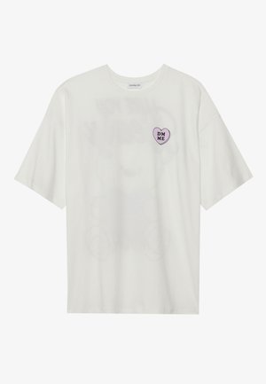 Witte T-shirt met korte mouwen met een kleine paarse hartafbeelding op de linkerborst met de tekst "DM ME" in zwarte letters.