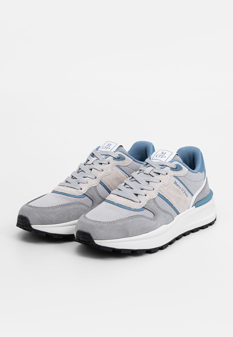 Grå sneakers med mesh- och mockamaterial. Har blå accenter, en vit sula och en strukturerad gummiyttersula. Snören och logotyp synliga.