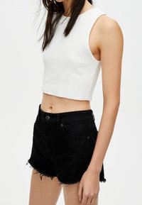 Top corto blanco de tirantes con textura acanalada, combinado con pantalones cortos de mezclilla negra de talle alto, que presentan un dobladillo deshilachado y bolsillos frontales.