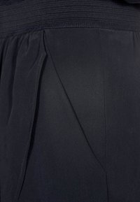 Gros plan d’un tissu noir montrant un détail de pli plié avec des bords cousus et une ceinture texturée sur un vêtement.