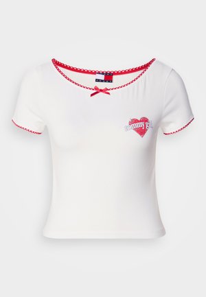 T-shirt bianco a maniche corte con bordi ondulati rossi e una piccola grafica a forma di cuore con il testo "tommy girl"; dettaglio a fiocco sul collo.