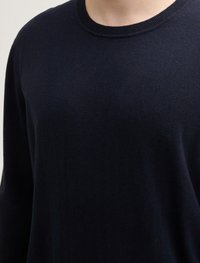 Pull léger en maille navy foncé avec un col rond, texture douce et design minimaliste. Aucune motif visible ni détails en matériel.