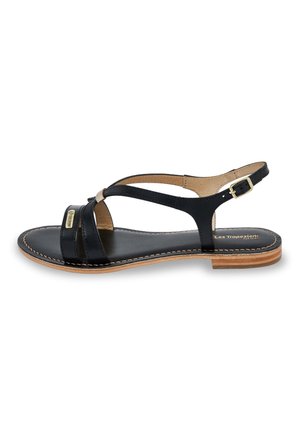 Black leather sandal featuring crossed straps, a low heel, and a gold-tone buckle detail. The sole is a light wood color with visible stitching.