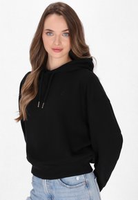 Felpa nera con cappuccio, dal taglio casual, con coulisse e maniche angolate, abbinata a jeans chiari strappati.