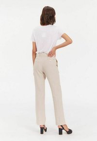 Pantalon beige clair avec une coupe droite, fabriqué à partir d'un tissu texturé. Présente une taille haute, des poches latérales et un design subtil de poche arrière.