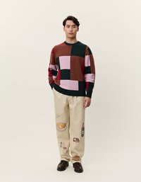 Multicolored gebreide trui met geometrische blokken in groen, roze, rood en bruin; gecombineerd met beige broeken met gedrukt voedselontwerp.