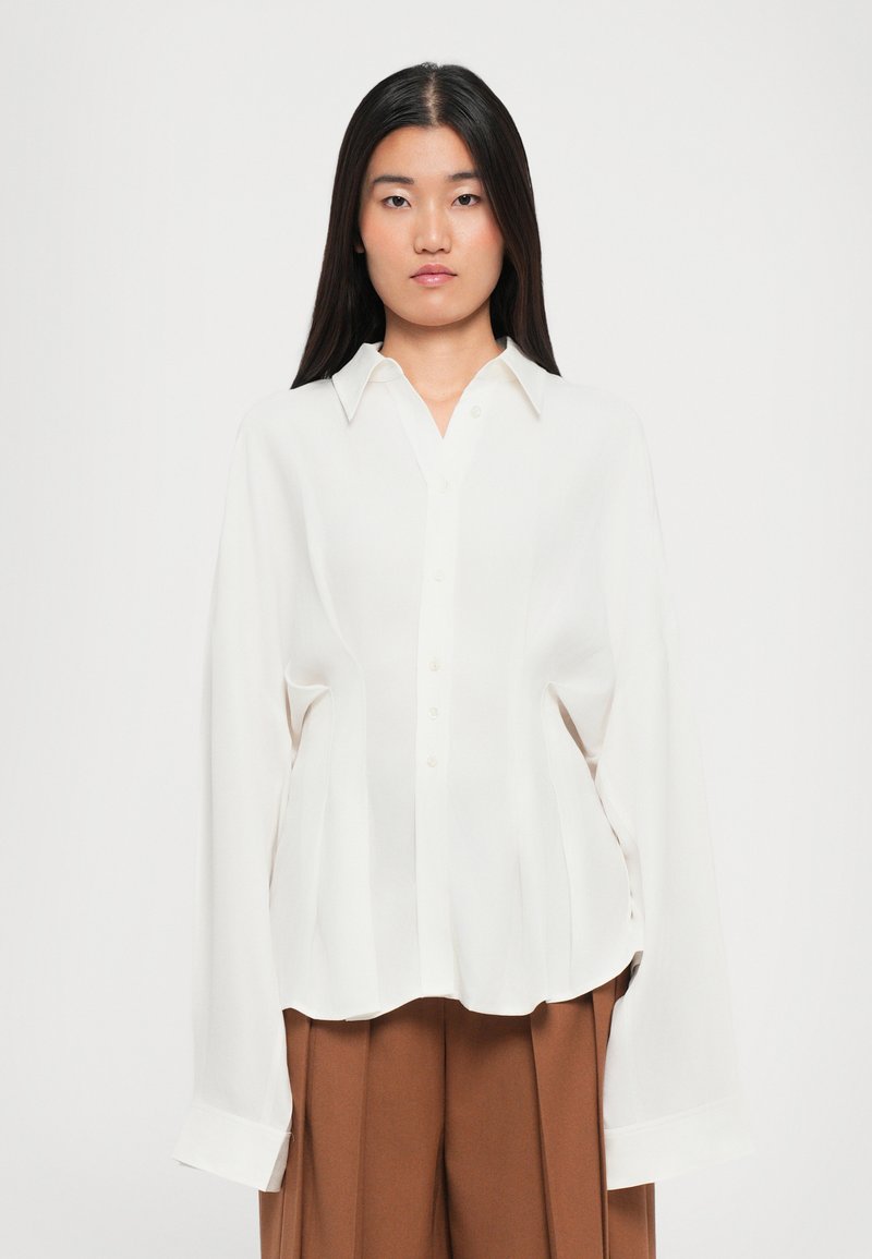 Cream-colored, lightweight blouse with a classic collar, button front, and long sleeves; features a relaxed fit and subtle pleats.