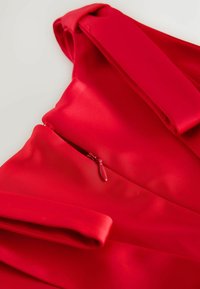 Rode stof met een gladde textuur, voorzien van een zijritsdetail en gestructureerde mouwen. Het ontwerp benadrukt een slanke, aansluitende silhouet.