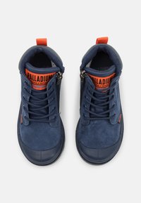 Modré polobotky s suede vrchním materiálem, gumovou špičkou, šněrováním vpředu a zipem. Obsahují jasně oranžové logo na jazyku a straně.