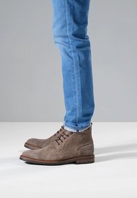 Bruine suède enkellaarzen met veters, met een gestructureerd oppervlak en een platte rubberen zool, gecombineerd met lichtblauwe spijkerbroek.