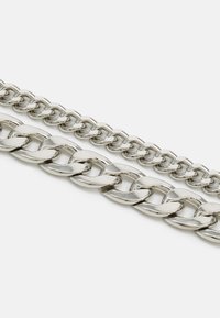 Metal chains in silver color, featuring a smooth, shiny surface. One chain is wider with rounded links, the other is thinner with hexagonal links.