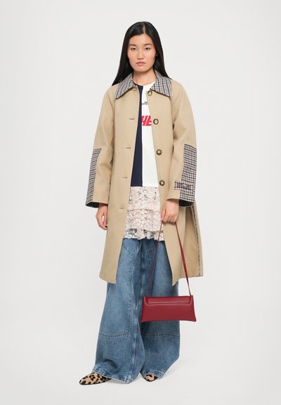 Beige trench coat with a houndstooth check collar and elbow patches, worn over a white shirt, lace top, and wide-leg denim jeans. Red handbag.