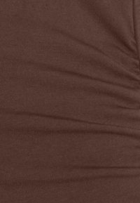Tissu marron avec une texture côtelée fine et des plis subtils, suggérant un matériau doux et extensible.