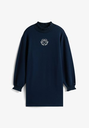 Robe sweat bleu marine avec un col haut à volants, des poignets élastiqués et un logo en forme de cœur brodé au centre. Confectionnée en tissu doux.