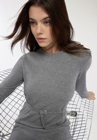 Szara sukienka z długim rękawem, wykonana z miękkiego materiału, z dopasowaną talią i paskiem oraz eleganckim, minimalistycznym wyglądem.