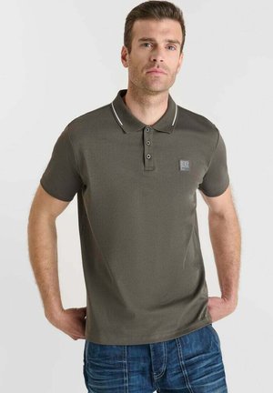 Polo olive avec des manches courtes, col côtelé, patte de boutonnage à trois boutons et un petit logo brodé ; associé à un jean en denim bleu.
