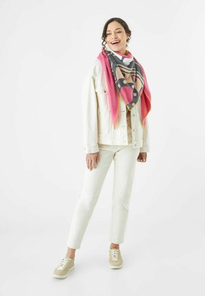 Multikleurige driehoekige sjaal met roze, grijze en beige patronen, gedragen over een wit denimjack en crèmekleurige broek.