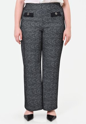 Donna che indossa pantaloni a vita alta neri e bianchi con trama, a gamba larga, con tasche decorative nere e scarpe nere con punta.
