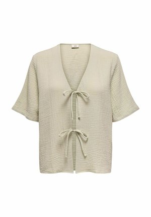 Blusa de color verde claro, texturizada, con mangas cortas, escote en V y cierre con lazo en el frente. Presenta un patrón de tela arrugada en toda su superficie.