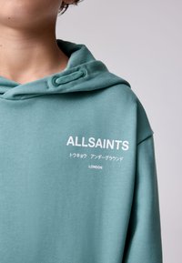 Menta zöld kapucnis pulóver texturált anyagból, fehér "ALLSAINTS" felirattal, valamint japán és "LONDON" feliratokkal az elején.
