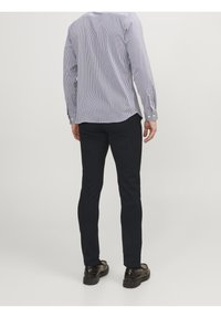 Pánská košile s dlouhým rukávem v modro-bílých pruzích, spárovaná s tmavými slim-fit kalhotami a černými botami. Košile má manžety na knoflíky a zakřivený lem.