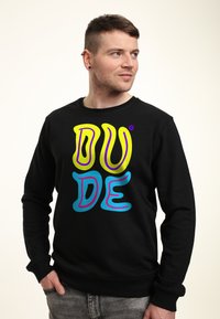 Sudadera negra con un gráfico de texto colorido "DUDE" en amarillo, azul y púrpura. Tejido suave con cuello redondo y puños de canalé.