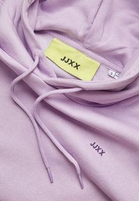 Lavendel hettegenser laget av myk stoff med snor. Har en gul etikett med "JJXX" og en liten "JJXX" trykt i lilla foran.