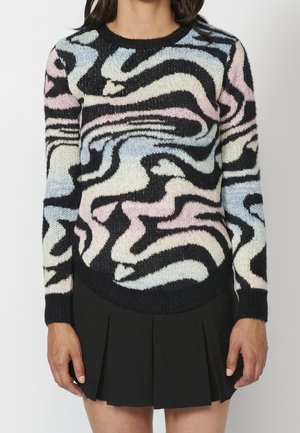 Femme portant une jupe noire et un pull à manches longues avec un motif tourbillonnant abstrait aux couleurs pastel bleu, rose et crème.