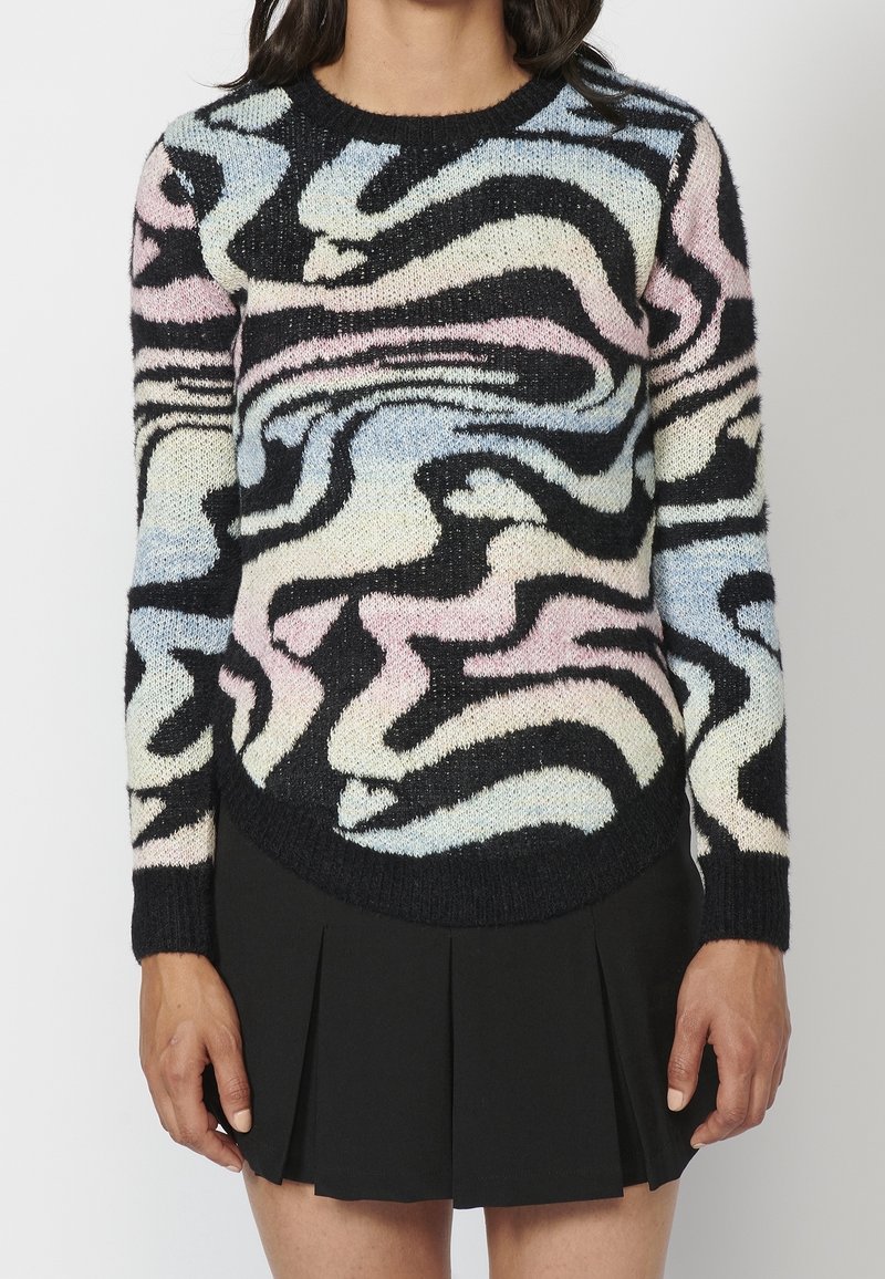Femme portant une jupe noire et un pull à manches longues avec un motif tourbillonnant abstrait aux couleurs pastel bleu, rose et crème.