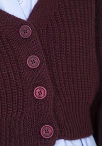 Cardigan lavorato a maglia borgogna con profondo scollo a V e quattro bottoni a contrasto. La trama è a coste, con un design aderente e colore uniforme.