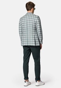 Marynarka w kratę w jasnoszarym, zielonym i granatowym kolorze; dopasowany krój z klapami. Połączona z ciemnozielonymi chinosami i białymi trampkami.