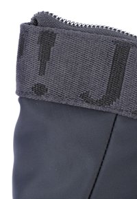 Svart vattentät känga med ett texturerat tygövre, som har en dragkedja och en mönstrad krage. Slät yta på den nedre delen.